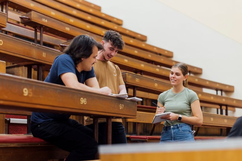Three students compare notes in lecture theatre