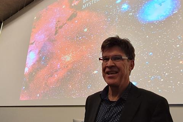 Evan Bieske standing in front of a screen displaying a colourful galaxy