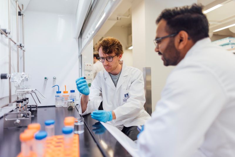 Two students inspect chemical specimen while seated at lab rangehood